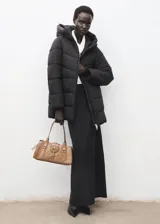 Campera acolchada tipo puffer color negro, con capucha, cuello alto y cierre frontal de cremallera doble. Presenta diseño recto, mangas largas con puños elásticos y bolsillos laterales con cierre.