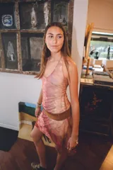 Vestido corto con estampado abstracto en tonos rosados, escote en V y breteles finos que se atan al cuello. Tiene corte en la cadera y falda con ruedo irregular y pico en lateral.