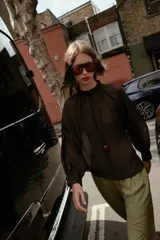 Blusa de cuello subido y manga larga abullonada con puños ajustados. Presenta un diseño semitransparente con textura arrugada y cierre frontal con botones a tono.