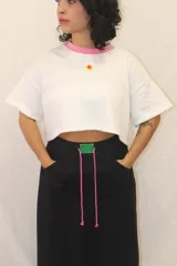 Remera corta de corte holgado en color blanco, con cuello redondo en color rosa y aplique decorativo de acrílico en el pecho.