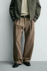Pantalón de corte baggy fit confeccionado en tejido de algodón con estructura diagonal y efecto lavado. Presenta cintura con pliegues frontales, bolsillos laterales, bolsillos traseros de vivo y un bolsillo lateral adicional con doble vivo en la pernera. Cierre frontal con cremallera y botón.