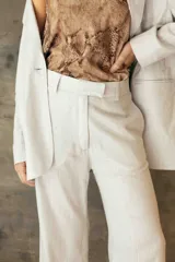 Pantalón sastrero de corte recto y tiro medio, confeccionado en tejido de lino con destellos de lurex, con cierre frontal y trabillas para cinturón.