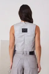 Chaleco de escote en V con cierre frontal mediante botones, bolsillos delanteros y estructura entallada en color plateado.