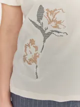 Remera negra de manga corta con cuello redondo y detalle de bordado floral en tono tostado en la parte inferior derecha.