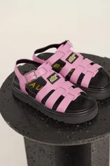 Sandalias de tiras anchas color crema con ajuste de hebilla al tobillo y suela track negra.