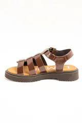 Sandalias cangrejeras de cuero marrón charol, estilo romano con múltiples tiras cruzadas, suela track plana y cierre de hebilla metálica ajustable en el tobillo.