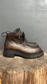 Bota acordonada de cuero con efecto desgastado, suela track de goma negra y costuras a la vista.