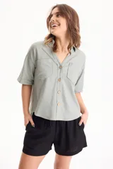 Camisa de lino color verde claro, de manga corta con vuelta, cuello camisero con escote en V, cierre frontal con botones de madera y dos bolsillos plaqué con solapa en el pecho.