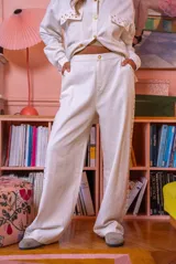 Pantalón de denim blanco de corte amplio, con cierre de botón y cremallera, y detalles de tachas en los laterales y bolsillos.