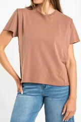 Remera de algodón color mostaza/naranja quemado, con cuello redondo y mangas cortas. Presenta un diseño con costuras externas visibles en los hombros y laterales, dándole un aspecto desestructurado.