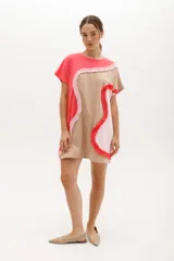 Vestido corto de algodón con diseño de bloques de color en tonos rosado, beige y fucsia. Presenta un corte relajado con cuello redondo, mangas raglán y detalles de volados aplicados en las costuras curvas que recorren la prenda.