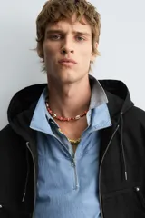 Cazadora negra de algodón con efecto lavado, corte relajado y capucha ajustable. Presenta cierre frontal de cremallera, bolsillos frontales tipo canguro y elásticos en puños y bajo.