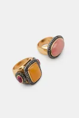 Pack de dos anillos metálicos dorados con piedras naturales y detalles de brillos. Uno presenta una piedra ovalada rosada y el otro una piedra rectangular naranja con aplicaciones laterales de resina.