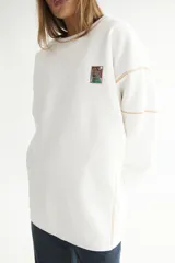 Buzo de algodón color blanco con efecto acid wash, cuello redondo y costuras a contratono color beige. Presenta un parche cuadrado con diseño gráfico en el pecho.