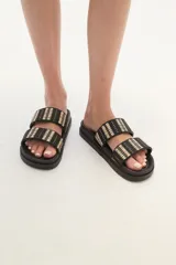 Sandalia tipo slide de color marrón, con doble tira ancha tejida en tonos tierra y negro, y suela anatómica de goma.