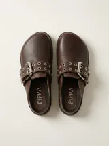 Zueco de cuero color chocolate, con diseño de punta redondeada y tira ajustable sobre el empeine con hebilla metálica y detalle de ojales decorativos.