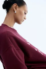 Buzo de tejido de punto color bordó, con cuello redondo y puños y bajo acanalados. Presenta un estampado frontal en blanco con el texto "RUNNING CLUB NEW YORK Central Park - Manhattan".