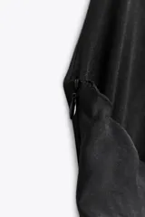 Vestido corto negro de tejido fluido con cuello halter que se ata con lazada. Tiene forro interior, detalle de frunces y bajo asimétrico con volantes. Cierre lateral con cremallera oculta.