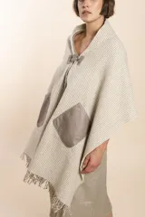 Chal de lana fina sin teñir con diseño de cuadros sutiles, cierre frontal con alamar y bolsillos de cuero metalizado. Presenta terminaciones con flecos en el ruedo y un calce estructurado en los hombros.