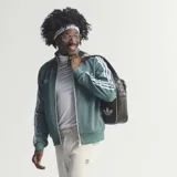 Campera deportiva Adidas Originals, modelo colaboración Bob Marley, color verde con las icónicas tres tiras blancas en las mangas. Presenta cuello alto, cierre frontal con cremallera y logo del Trifolio bordado en el pecho.