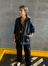 Campera negra con capucha, cierre frontal con cremallera dorada, bolsillos laterales y puños elásticos.