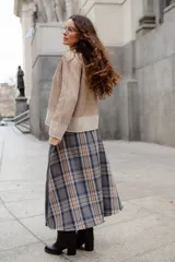 Falda midi de diseño asimétrico que combina paño gris liso con un panel lateral de tela escocesa en tonos grises, marrones y blancos. Presenta un corte irregular con bordes desflecados y tajos laterales.