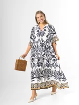 Maxi vestido blanco con estampado paisley en azul marino y detalles en tonos dorados, con cuello en V, mangas amplias y diseño escalonado.