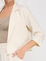 Blazer corto de lino color beige, marca Allie Rose, de estilo relajado y corte crop con frente abierto sin botones. Presenta solapa de muesca y mangas tres cuartos con detalle fruncido en los laterales.