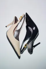 Zapato de tacón destalonado color negro charol, con tira trasera ajustable con hebilla metálica dorada y punta fina. Tacón aguja de 8 cm de altura.