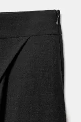 Pantalón negro de tiro alto con diseño cruzado tipo pareo, pinzas delanteras y pernera ancha. Cuenta con cierre lateral de cremallera oculta.