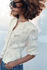Chaqueta de cuello redondo y manga por debajo del codo con tejido combinado, color crudo, con cierre frontal con botones y detalles bordados.