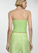 Top corto tipo palabra de honor en color verde lima, con diseño entallado, espalda con panel nido de abeja y detalle drapeado en los laterales. Cuenta con cierre de cremallera en la parte posterior y forro interior.