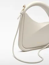 Bolso de cóctel en color blanco roto con estructura rígida y diseño geométrico. Cuenta con un asa tubular corta integrada y una correa larga extraíble. Presenta cierre magnético y un compartimento principal.