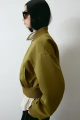 Campera bomber de tejido grueso color verde militar, con cuello corto acanalado, cierre frontal y bolsillos insertados. Cuenta con hombros caídos, mangas abullonadas y puños y bajo acanalados.