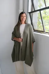 Poncho abierto de tejido de punto color verde oliva, con mangas cortas tipo kimono y bolsillos frontales aplicados.