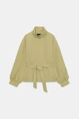Cazadora de color verde militar, con cuello alto, manga larga abullonada con puños y cierre frontal con botones a presión ocultos. Incluye un cinturón ajustable del mismo tejido para entallar la cintura y bolsillos delanteros de vivo.