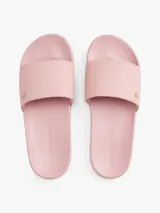 Ojotas tipo slide color rosa pálido, con pala ancha que presenta un patrón de monograma TH en relieve. Cuentan con una pequeña insignia metálica dorada del monograma TH en la tira y el logo de Tommy Hilfiger en relieve en la entresuela.