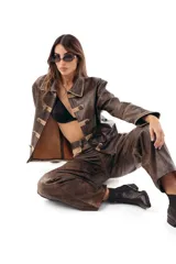 Campera estilo militar napoleón confeccionada en cuero ovino, con cierre frontal y solapa decorativa con botones metálicos y alamares de gamuza en tono crudo. Cuenta con cuello camisero, pespuntes visibles y diseño estructurado de manga larga.