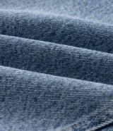 Pantalón de jean con corte balloon de gran volumen en las piernas, diseño de tiro medio con pasacintos, bolsillos laterales inclinados y cierre frontal con botón y cremallera. Presenta detalles de botones aplicados en los puños.