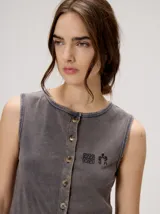 Musculosa MUTMA Trebola de silueta recta confeccionada en tejido de punto color gris con efecto lavado. Posee cierre frontal con botones, detalle de bordado en el pecho y terminación festoneada en el ruedo y las sisas.