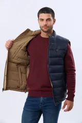 Chaleco reversible acolchado con diseño capitoneado. Un lado presenta un acabado en color beige con cierre frontal y bolsillo vertical en el pecho, mientras que el otro lado es de color azul marino. Cuenta con cuello alto y relleno térmico para mayor abrigo.