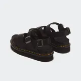 Sandalias Dr. Martens modelo Voss II, color negro, con tiras cruzadas en el empeine, correas ajustables con hebilla en el talón y tobillo, suela flatform dentada de EVA con el inconfundible pespunte amarillo de la marca.