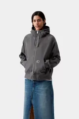 Campera con capucha de corte holgado, color gris oscuro efecto desgastado, con cierre frontal completo, cuello alto, bolsillos tipo canguro y mangas raglán. Presenta una pequeña etiqueta cuadrada con el logo de la marca en el bolsillo izquierdo.