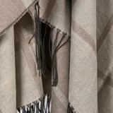 Poncho abierto de tejido de punto con diseño de cuadros grandes en tonos beige y marrón, con terminaciones de flecos en el ruedo.