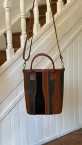 Matera de cuero con diseño de paneles verticales en combinación de colores azul, verde, marrón y bordó. Cuenta con dos asas cortas de cuero y estructura rígida.