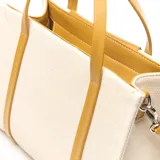 Cartera tipo tote de material textil color beige con detalles y asas en cuero sintético color mostaza. Cuenta con un bolsillo externo frontal con cierre y el logo de la marca impreso, doble asa de mano y correa de hombro ajustable y desmontable.