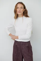 Polera de manga larga en color blanco, confeccionada en tejido texturizado con cuello alto tipo mock neck y detalle de volados en el borde.