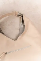 Bolso de hombro color beige, confeccionado en cuero sintético con interior plateado. Presenta un bolsillo externo con cierre.