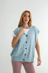 Chaleco de punto color verde, con escote en V y cierre frontal de botones negros. Presenta un diseño holgado con terminaciones acanaladas en el cuello, sisas y ruedo.