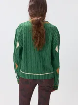 Sweater de punto con diseño de ochos en color verde, cuello redondo con detalle de franja en contraste, y apliques de rombos en las mangas. Presenta un bordado con la letra M en el pecho.